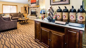 A living room with a fireplace, a sofa, a coffee station, and a patterned carpet. - AmericInn by Wyndham Menomonie (Menomonie)