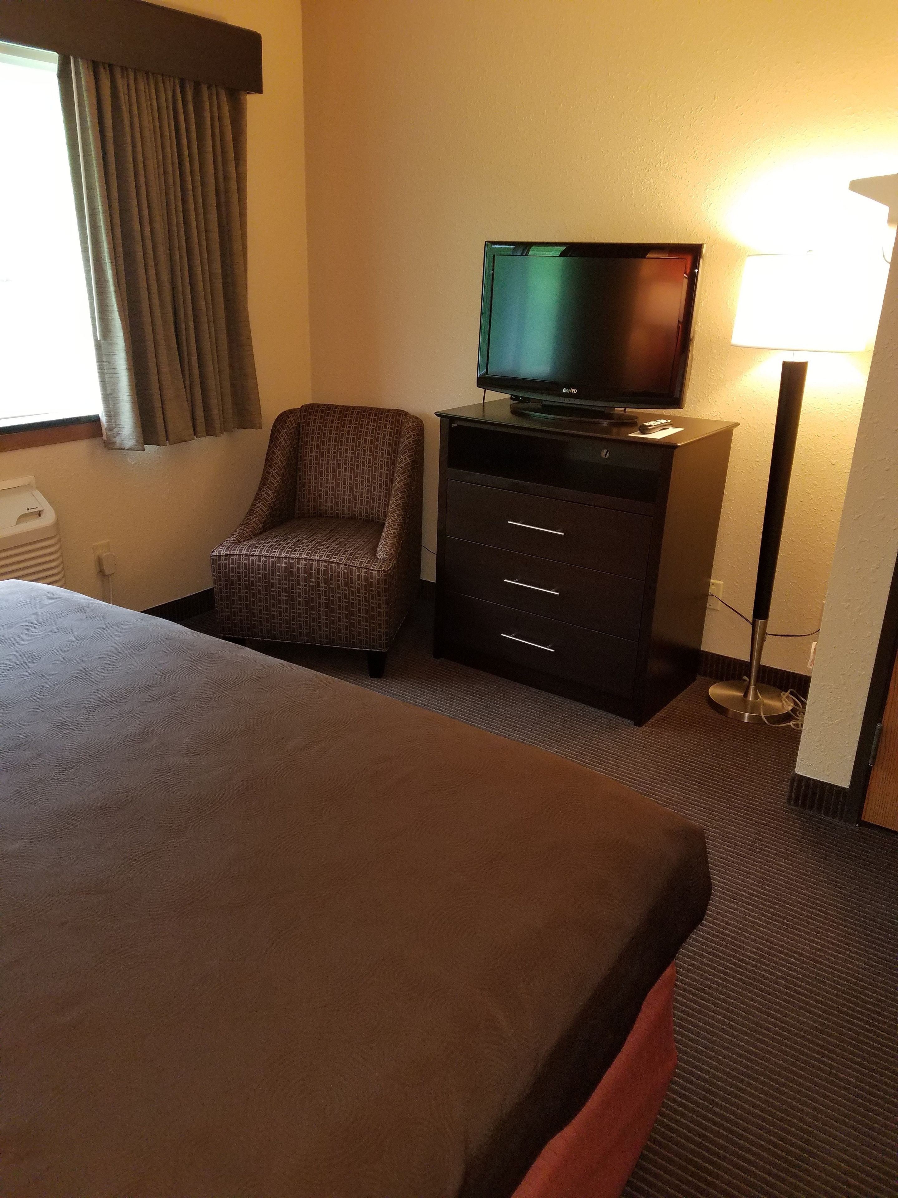 Een hotelkamer met een bed, een televisie op een dressoir, een stoel en een lamp.