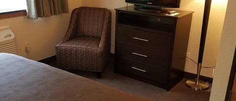 A hotel room with a bed, a television on a dresser, a chair, and a lamp.