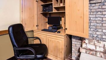 Un escritorio de madera con una computadora, una silla negra y una impresora sobre estanterías.