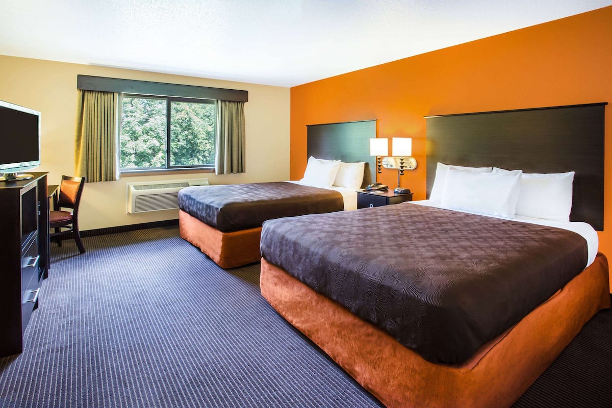A hotel room with two beds, a desk with a TV, and a window with curtains.