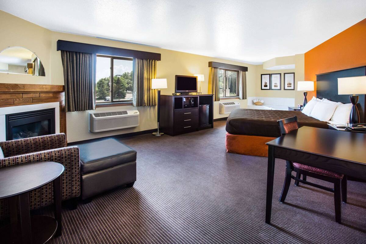A hotel room with a bed, a desk, a chair, a sofa, a TV, and a fireplace.