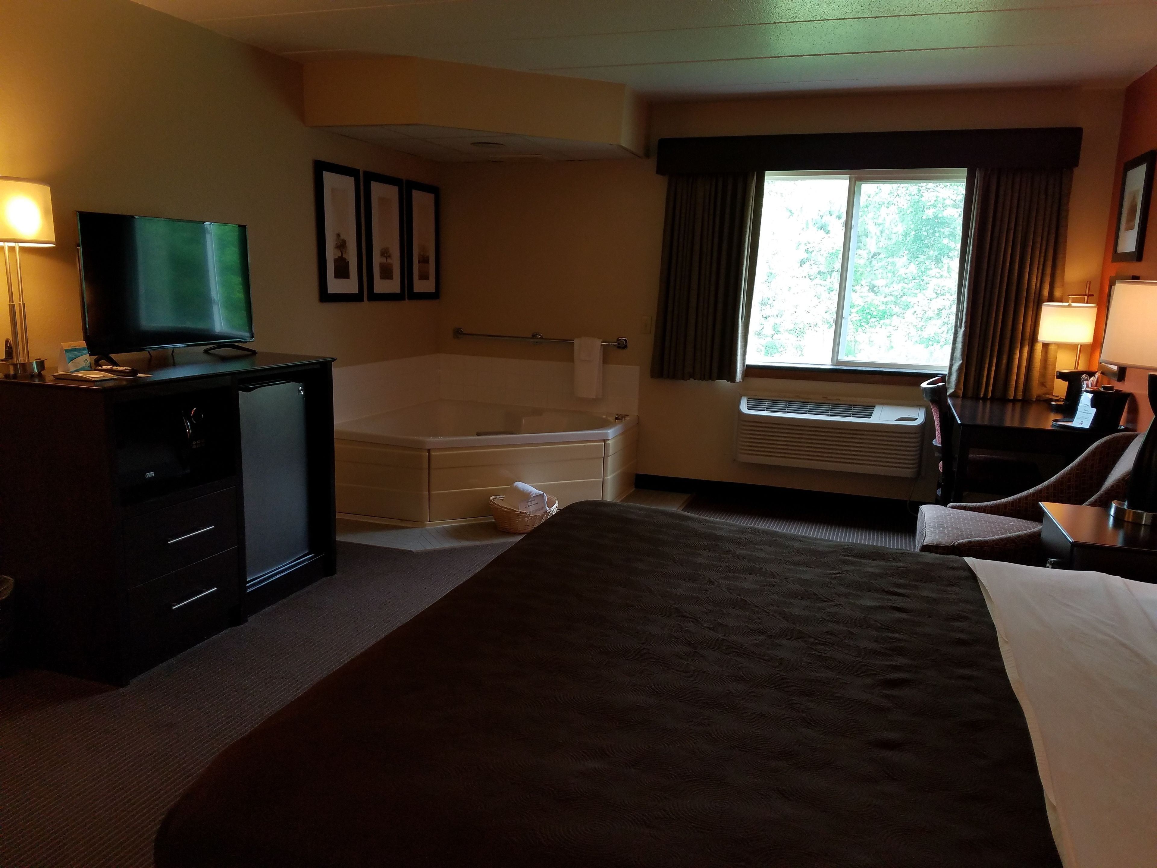 A hotel room with a bed, a desk, a television, a bathtub, and a window with curtains.