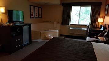 A hotel room with a bed, a desk, a television, a bathtub, and a window with curtains.