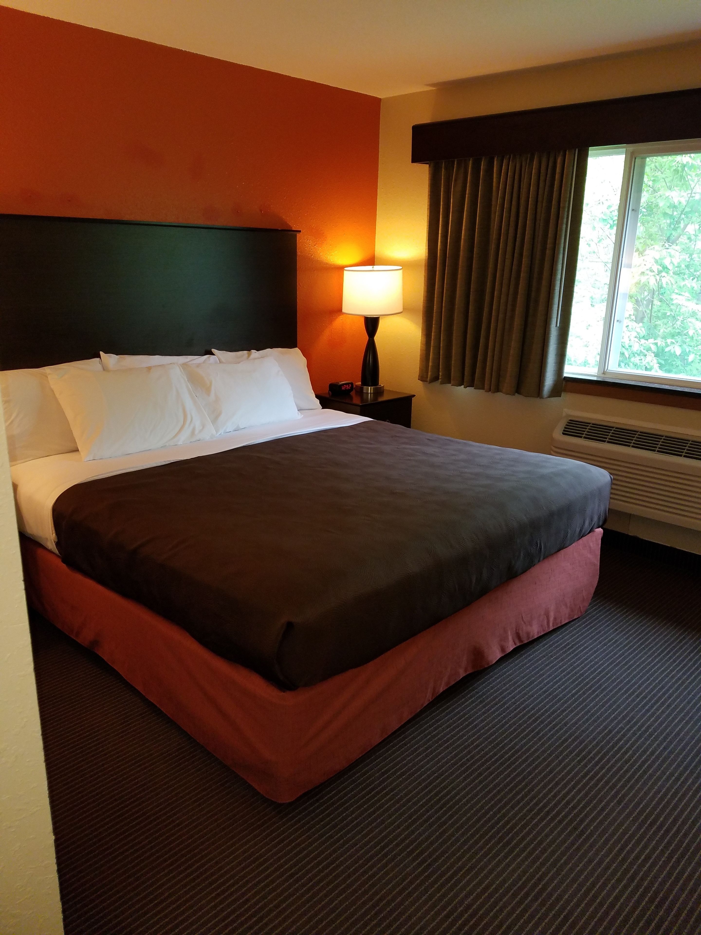 Ein Hotelzimmer mit einem großen Bett, einer Nachttischlampe, einem Fenster mit Vorhängen und einer Klimaanlage.
