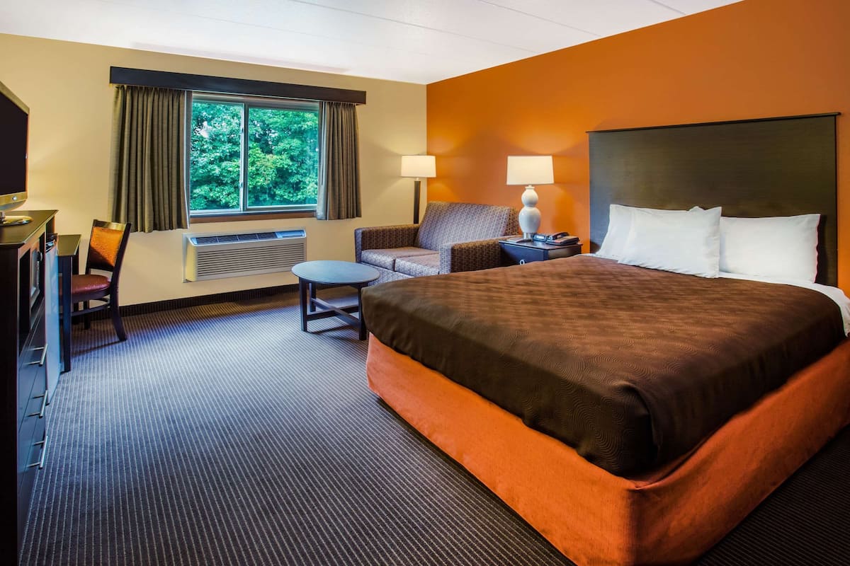 A hotel room with a large bed, a desk, a chair, a small table, and a window with curtains.