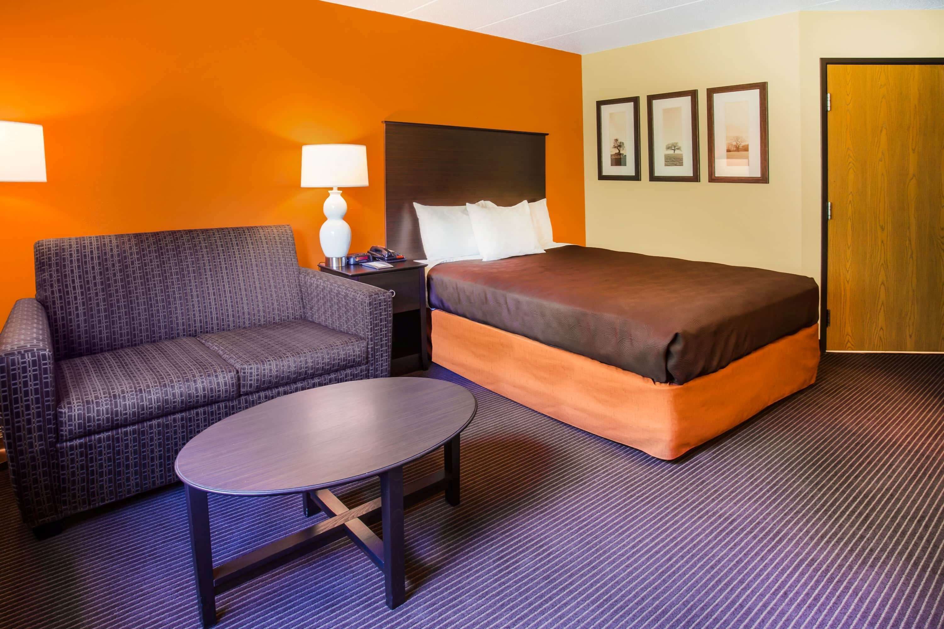 A hotel room with a bed, a sofa, a small table, and a nightstand with a lamp.