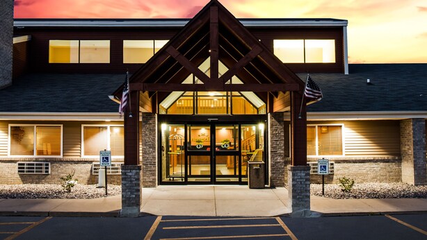 A hotel entrance with a covered walkway, a parking lot, and a sunset sky. - AmericInn by Wyndham Menomonie (Menomonie)