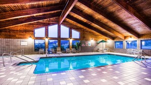 An indoor swimming pool with a wooden ceiling and tiled floor, surrounded by windows and chairs. - AmericInn by Wyndham Menomonie (Menomonie)
