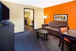 Una habitación de hotel con televisión, sofá, mesita y mesa de comedor.