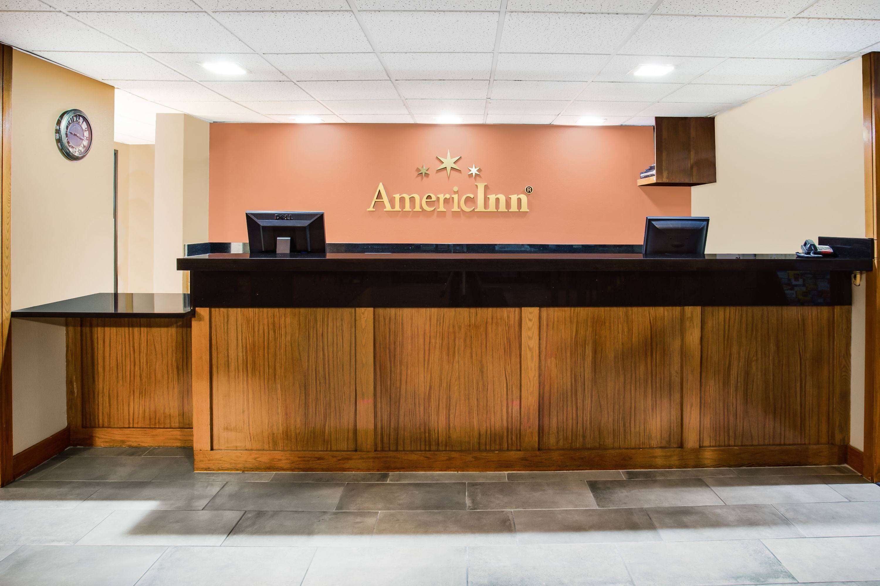 Een receptiebalie met het AmericInn logo, een klok aan de muur en een houten paneelwand.