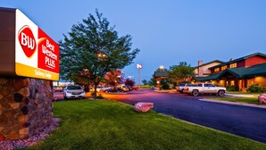 A hotel entrance with a large sign for Best Western Plus, a stone wall, and a parking lot with cars. - Best Western Plus Sidney Lodge (Sidney)