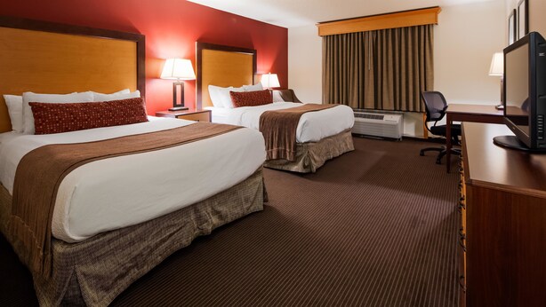 A hotel room with two beds, a desk with a computer, and an air conditioning unit. - Best Western Plus Sidney Lodge (Sidney)
