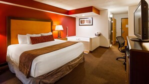 A hotel room with a large bed, a desk, a chair, a TV, a bathroom, and a framed picture on the wall. - Best Western Plus Sidney Lodge (Sidney)