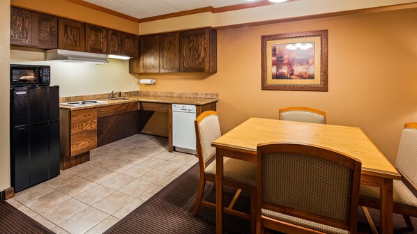 Una cocina compacta con armarios de madera, un refrigerador negro, lavavajillas y una zona de comedor con mesa de madera y sillas acolchadas.