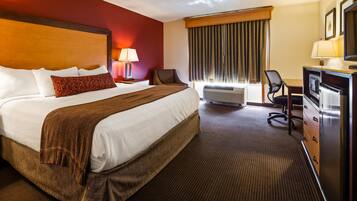 Une chambre d’hôtel avec un grand lit, un bureau avec une télévision, une chaise et une lampe.