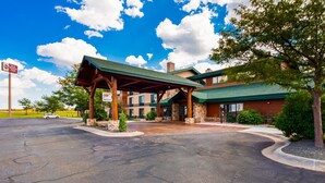 A hotel entrance with a covered driveway, stone pillars, and a large building with a green roof. - Best Western Plus Sidney Lodge (Sidney)