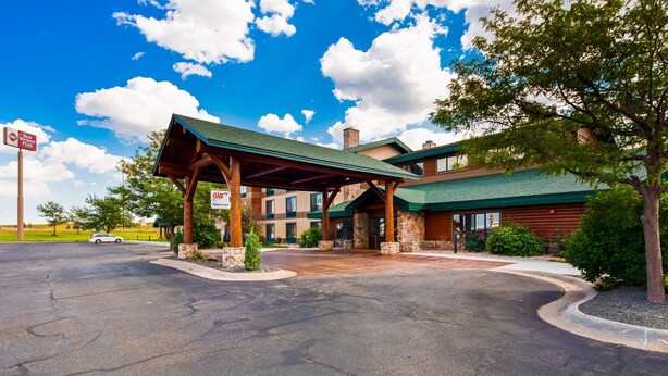 A hotel entrance with a covered driveway, stone pillars, and a large building with a green roof. - Best Western Plus Sidney Lodge (Sidney)