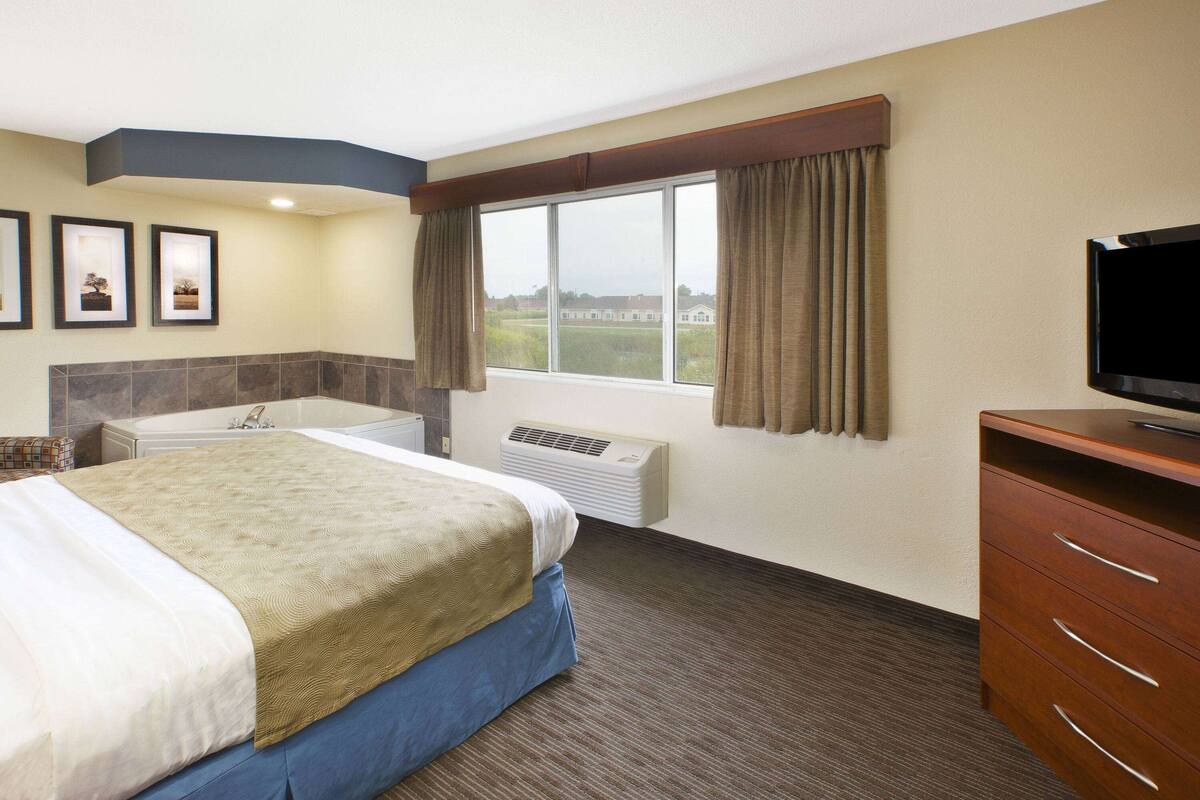 Une chambre d’hôtel avec un grand lit, une télévision, une salle de bain avec baignoire et une fenêtre avec des rideaux.