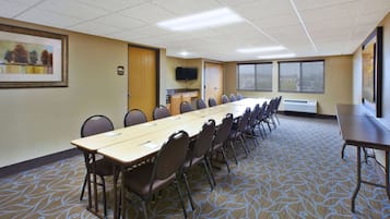 A conference room with a long table, chairs, a television, and windows with blinds.
