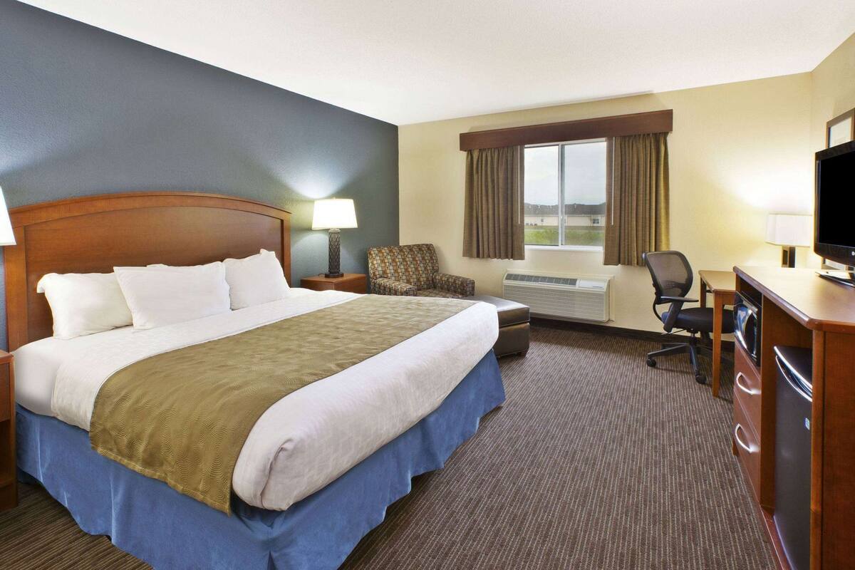 Une chambre d’hôtel avec un grand lit, un bureau avec un ordinateur, une chaise, une télévision et une fenêtre avec des rideaux.