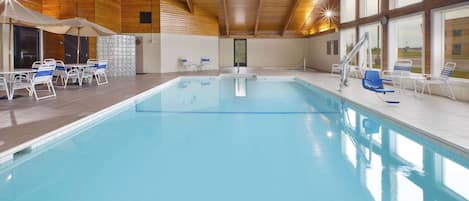 An indoor swimming pool with a wooden ceiling, tiled walls, and a view of the outside.