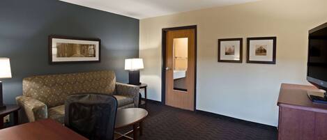 A hotel room with a sofa, armchair, small round table, and a television on a cabinet.
