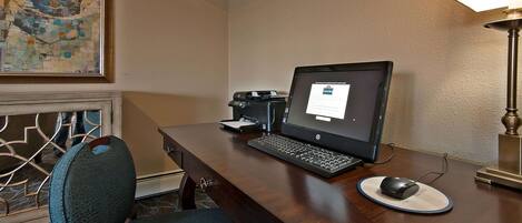 A hotel room with a wooden desk, a laptop, a desktop monitor, a mouse, a lamp, and a chair.