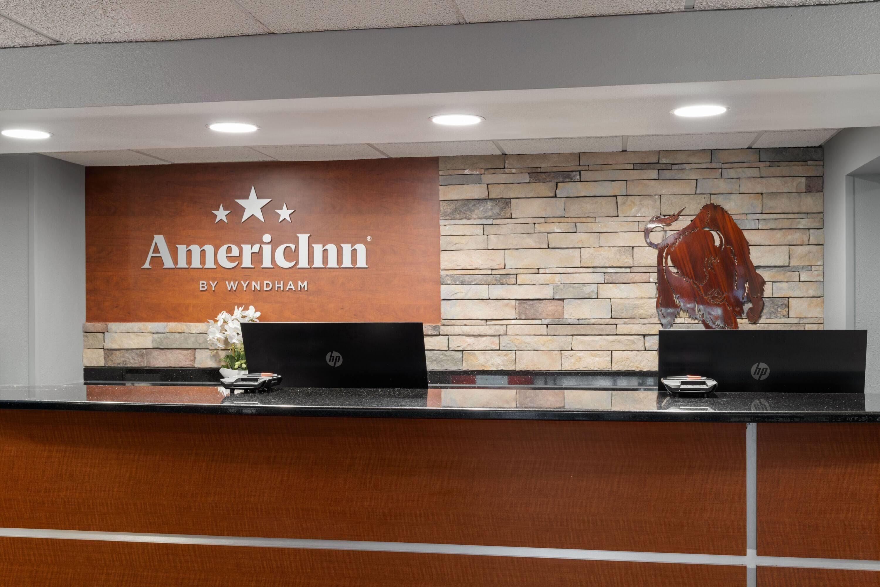 A reception desk with a sign reading "American Inn by Wyndham" and a stone wall with a decorative metal sculpture.