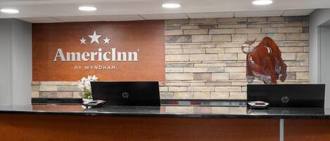 A reception desk with a sign reading "American Inn by Wyndham" and a stone wall with a decorative metal sculpture.