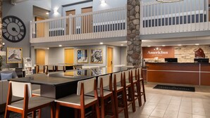 A spacious lobby with a long reception desk, multiple seating areas, and a clock on the wall. - AmericInn by Wyndham Grand Forks (Grand Forks)