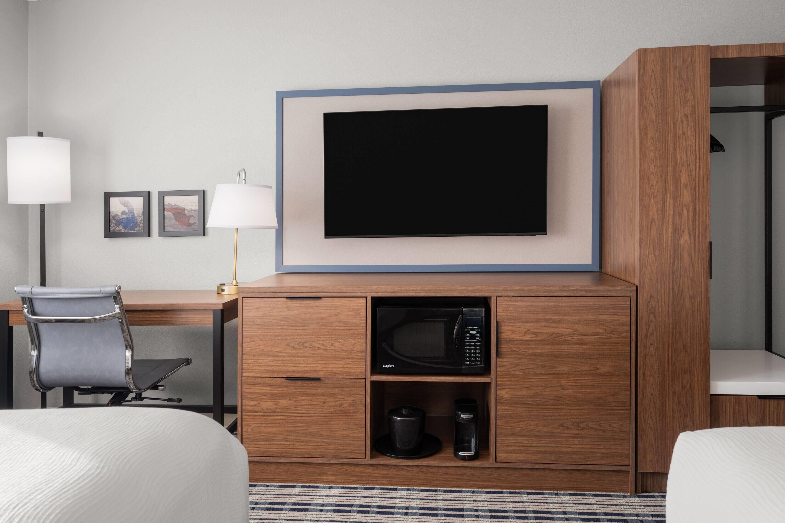 A hotel room with a bed, a desk, a chair, a television mounted on the wall, a microwave, and a coffee maker.