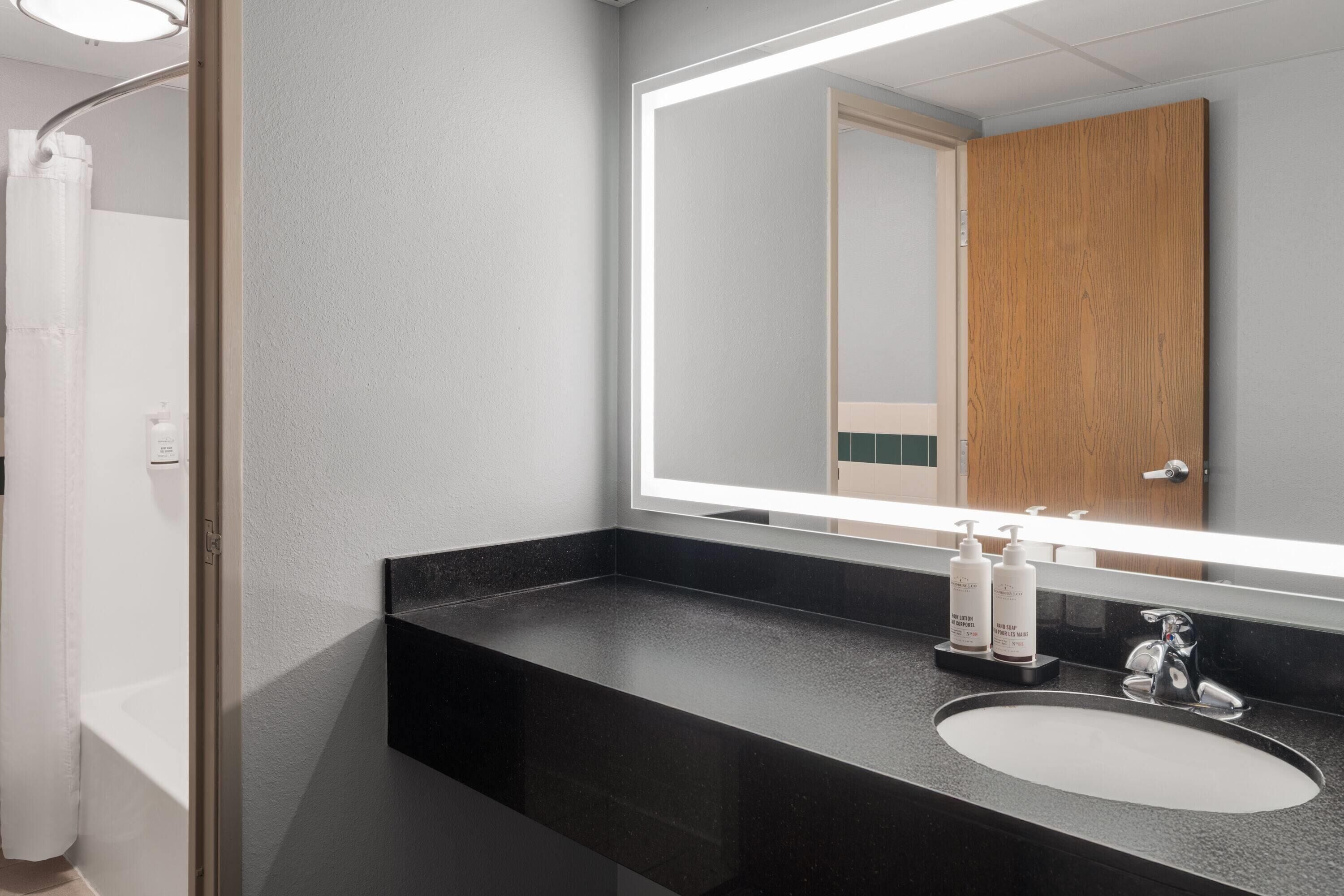A modern bathroom with a black countertop, a white sink, and a large mirror.