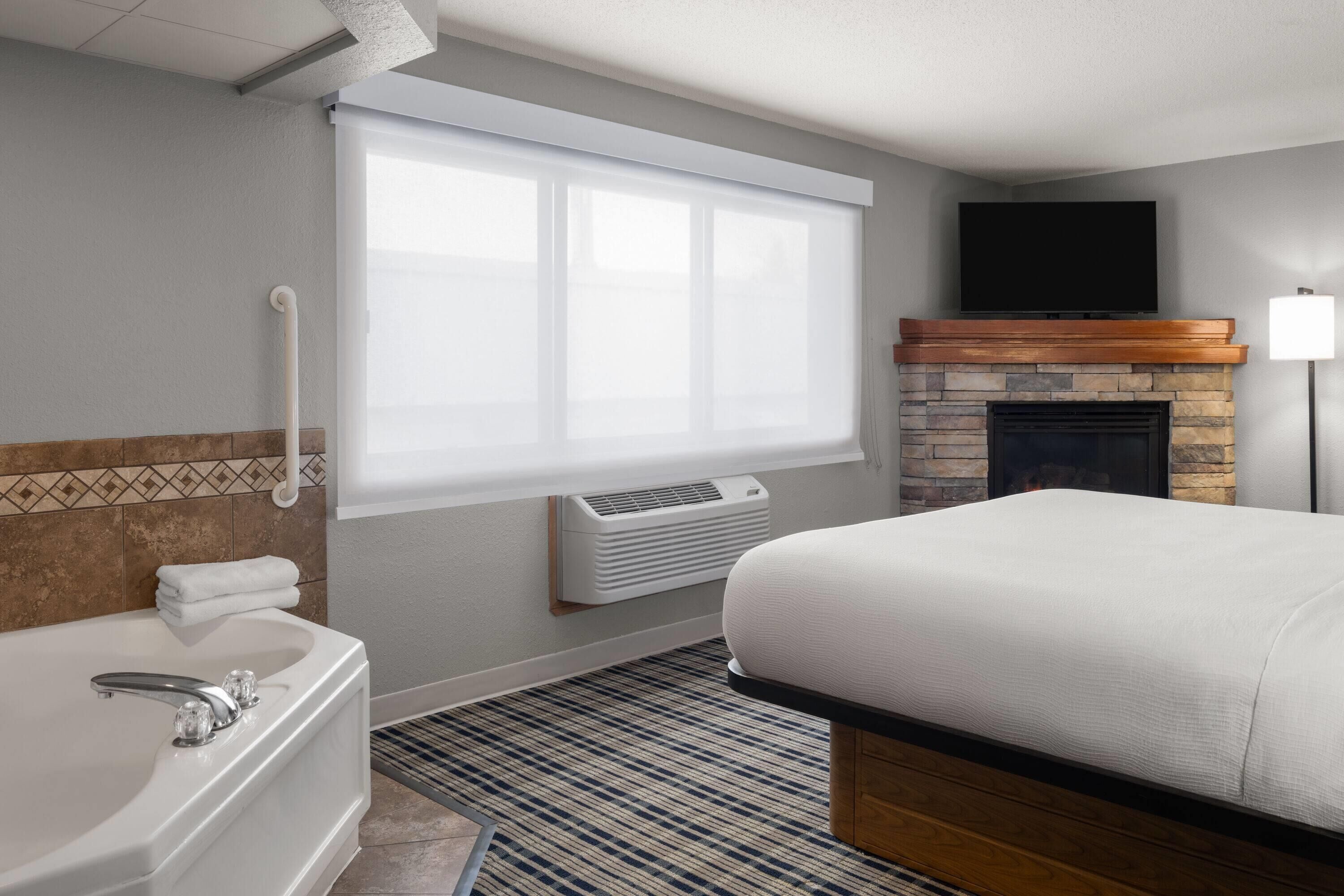 A hotel room with a large bed, a bathtub, a fireplace, and a television on the wall.