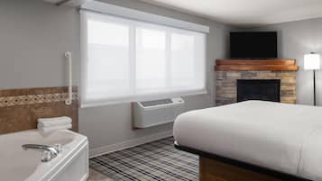 A hotel room with a large bed, a bathtub, a fireplace, and a television on the wall.