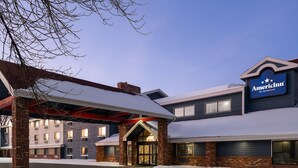 A hotel entrance with a covered walkway, brick facade, and a sign for 'American Inn by Wyndham'. - AmericInn by Wyndham Grand Forks (Grand Forks)