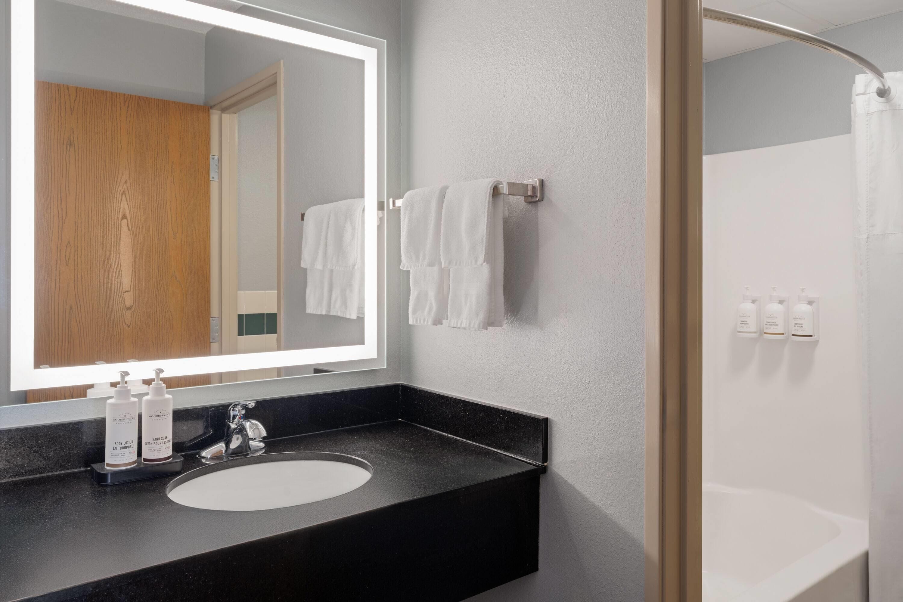 A modern bathroom with a black countertop, a large mirror, and a glass shower enclosure.