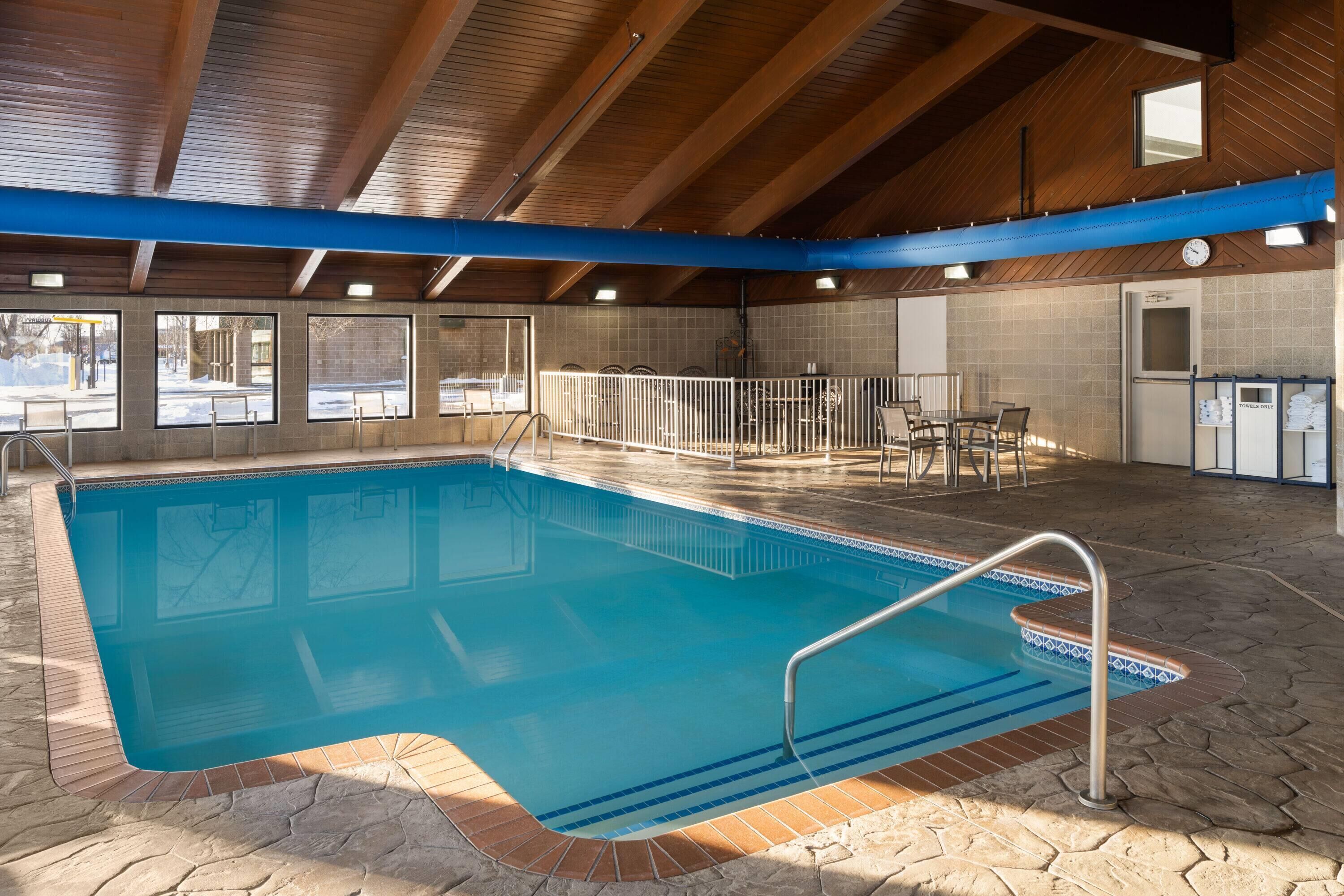 Una piscina interior con suelo de baldosas, techo de madera y vistas al exterior a través de amplios ventanales.