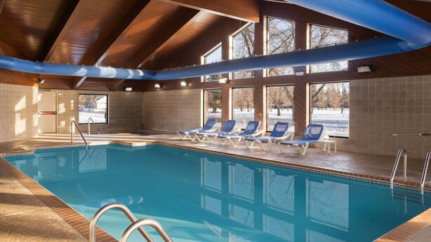 An indoor swimming pool with clear blue water, wooden ceiling beams, and a tiled floor. - AmericInn by Wyndham Grand Forks (Grand Forks)