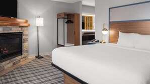 A hotel room with a large bed, a fireplace, a wardrobe, and a television. - AmericInn by Wyndham Grand Forks (Grand Forks)