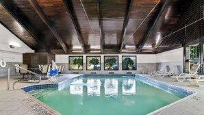 Una piscina interior con suelo de baldosas, techo de madera y vistas a árboles a través de grandes ventanales.