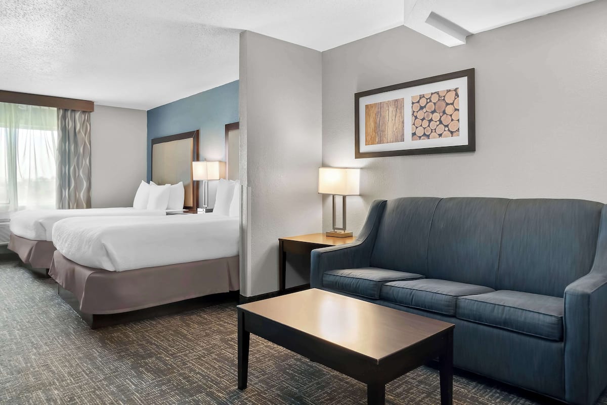 A hotel room with two beds, a sofa, a coffee table, and a wall-mounted lamp.