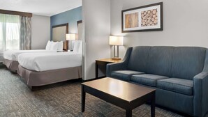 Habitación de hotel con dos camas, un sofá, una mesita de café y una lámpara de pared.