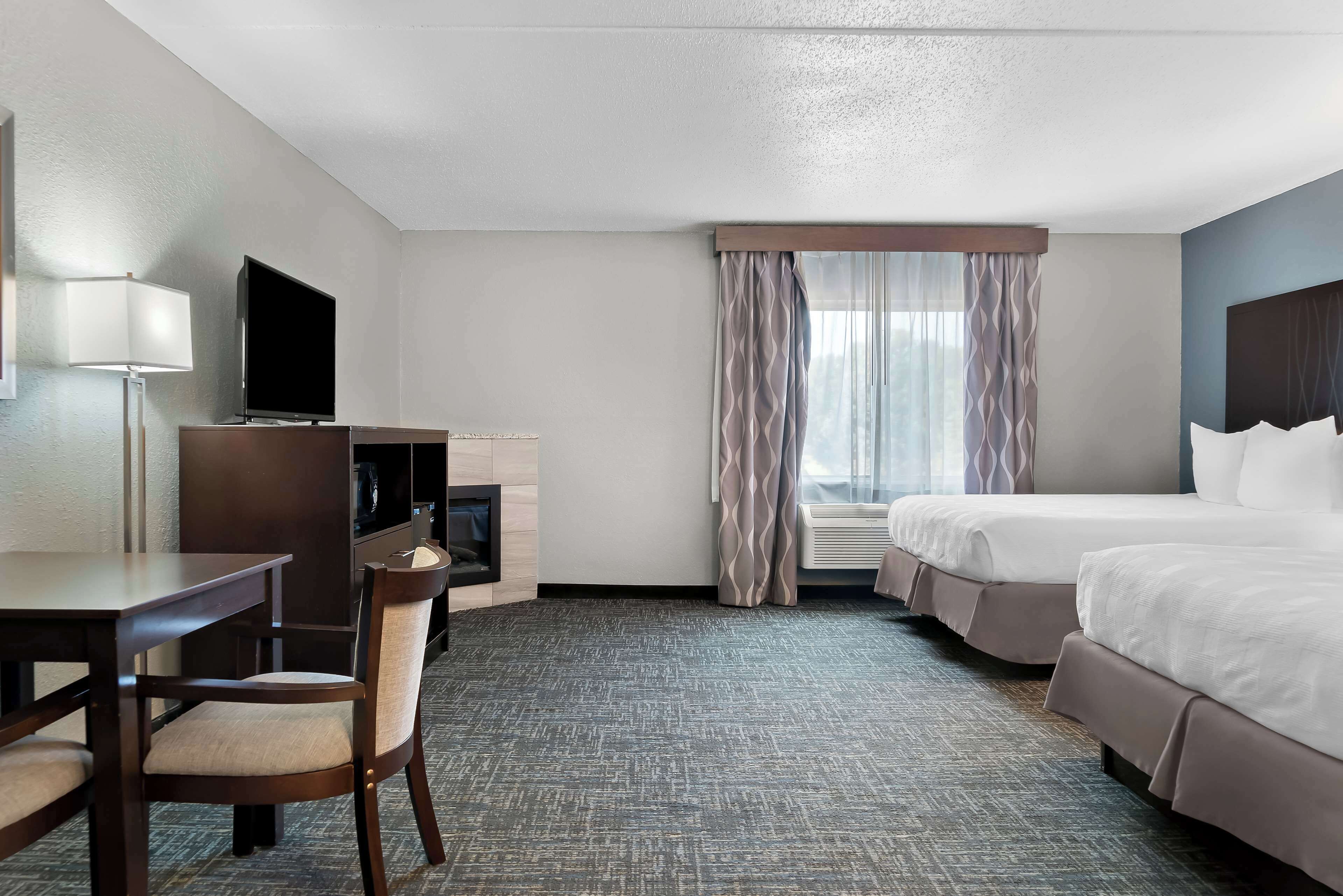 Una habitación de hotel con cama, escritorio, silla, televisor y ventana con cortinas.