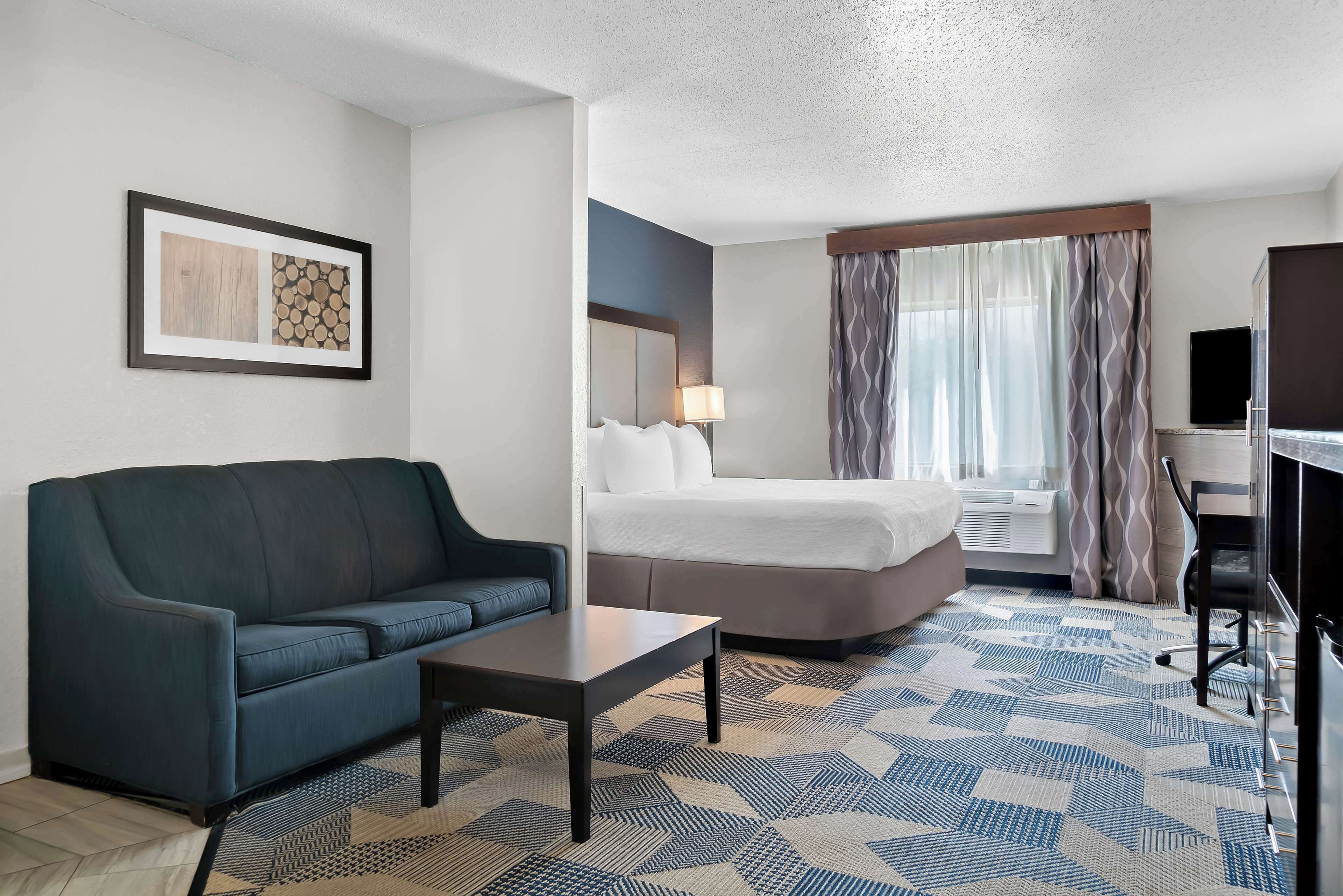 Une chambre d’hôtel avec un canapé, un lit, un bureau et une grande fenêtre avec des rideaux.