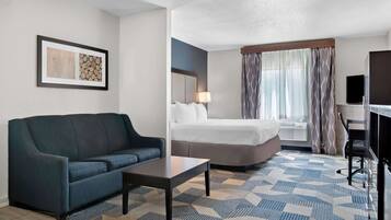 Une chambre d’hôtel avec un canapé, un lit, un bureau et une grande fenêtre avec des rideaux.
