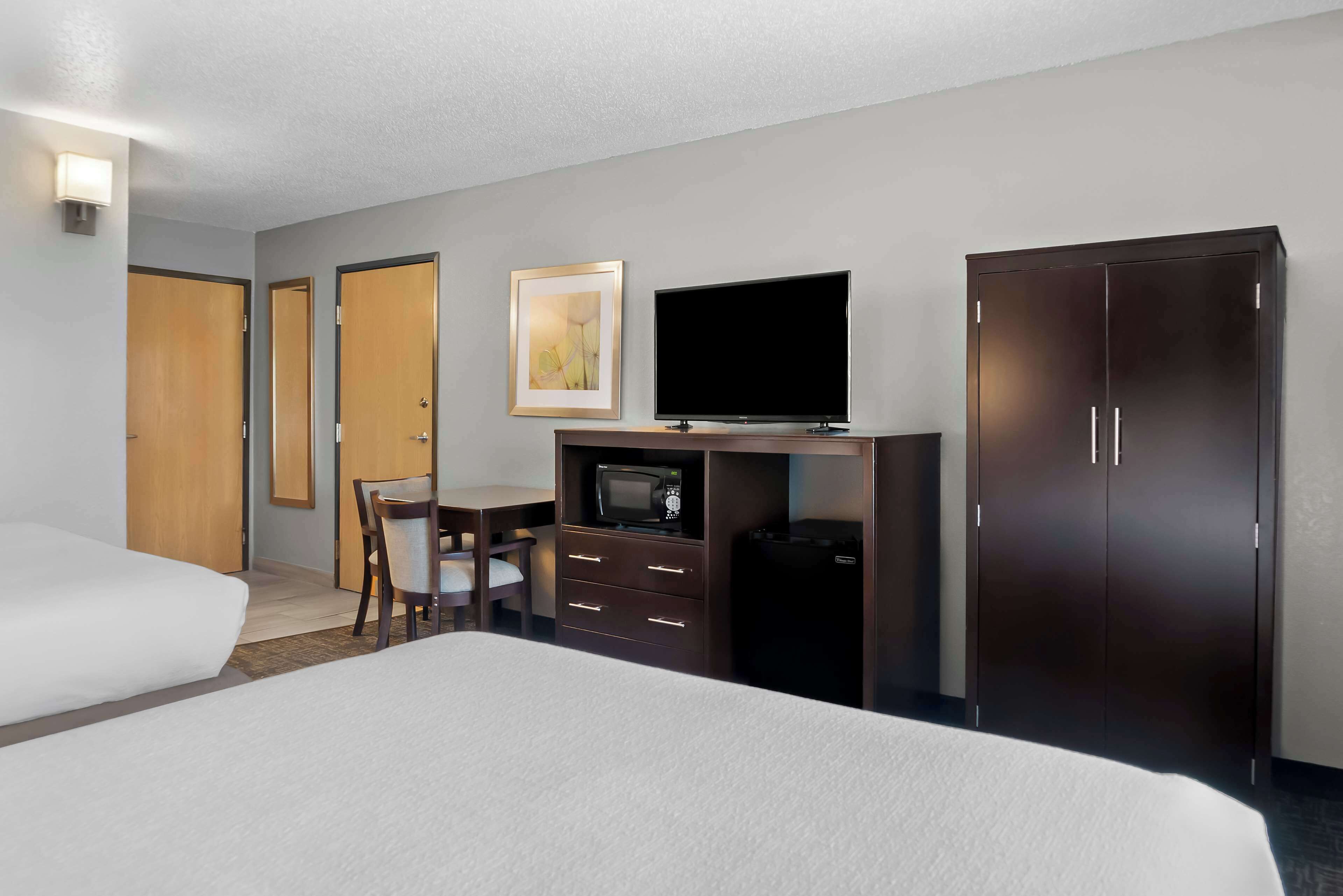 Habitación de hotel con dos camas, un escritorio con silla, televisión, microondas, armario y un cuadro en la pared.