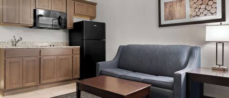 A compact living space with a kitchenette, a gray sofa, a wooden coffee table, and a framed picture on the wall.