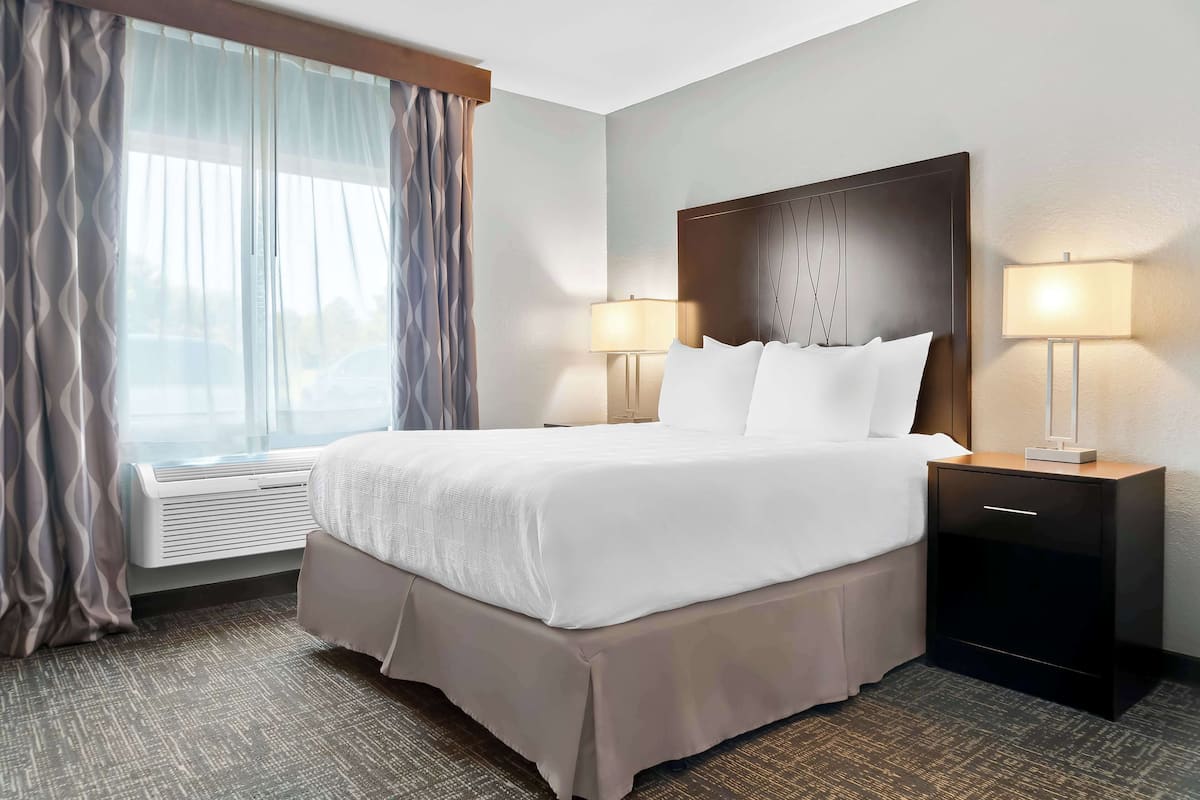 A hotel room with a large bed, two bedside lamps, a nightstand, and a window with curtains.