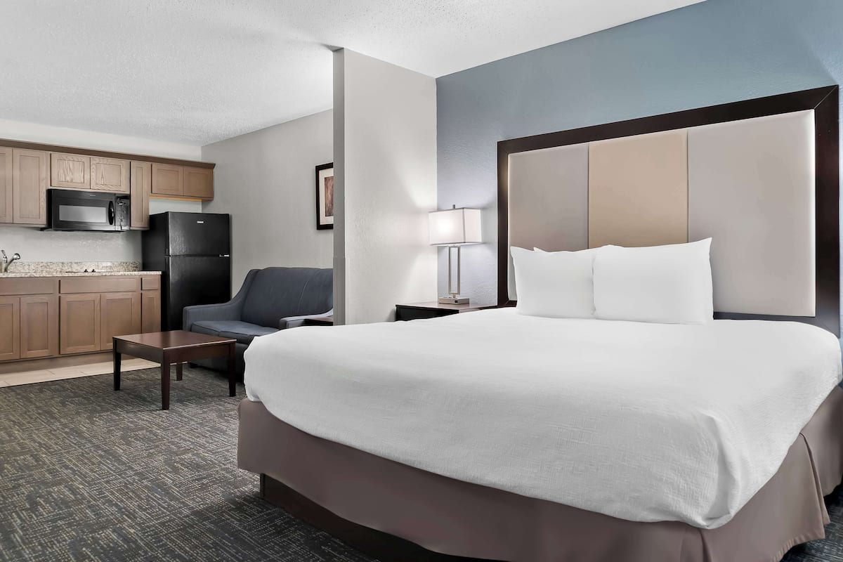 A hotel room with a large bed, a desk, a chair, a microwave, and a refrigerator.